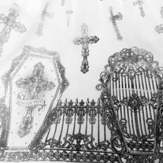 black and white photograph of an ornate iron fence with crosses on it, in front of a wall