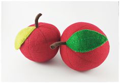 two red apples with green leaves on them sitting next to each other in front of a white background