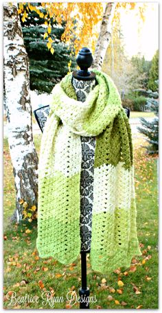 a green and white scarf sitting on top of a mannequin next to a tree