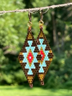 a pair of beaded earrings hanging from a rope in front of some green trees