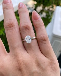 a woman's hand with a diamond ring on top of her finger and an object in the background