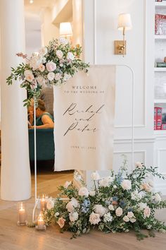 a welcome sign with flowers and greenery on the floor in front of some candles