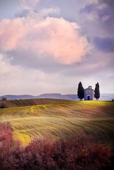 an image of a house in the middle of a field with trees and clouds above it