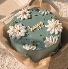 a blue cake with white flowers and the words happy written on it in gold lettering