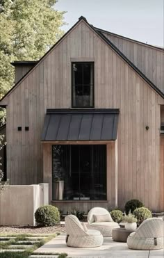 two wicker chairs sitting in front of a wooden house with black roof and windows