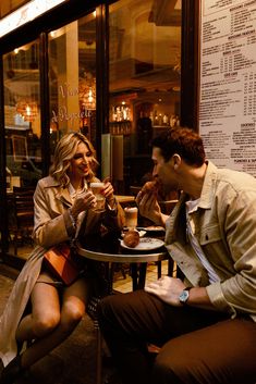 a man and woman sitting at a table in front of a window eating food together