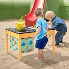 two young boys playing in the sand at a play area with a table and slide