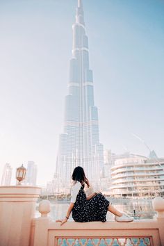 a woman is sitting on a ledge looking at the burjt in the background