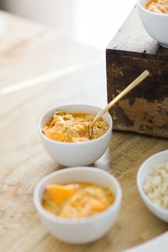 three bowls of food sitting on top of a wooden table next to rice and bread