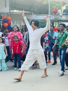 a man is dancing in the middle of a group of people with balloons behind him