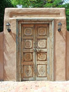 an old wooden door in front of a adobe building with decorative carvings on the doors