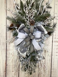 a christmas wreath hanging on the side of a white wooden wall with snow and pine cones