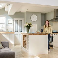 a woman standing in the middle of a kitchen with white cabinets and an island counter