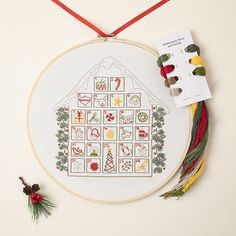 a cross stitch christmas house is displayed on a white surface with red ribbon and other items