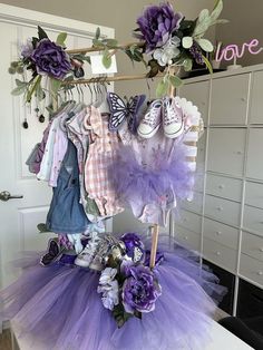 there is a purple tutu and some flowers on the clothes rack in this room