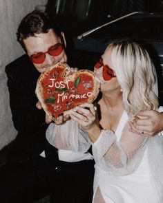 a man and woman kissing while holding up a heart shaped pizza