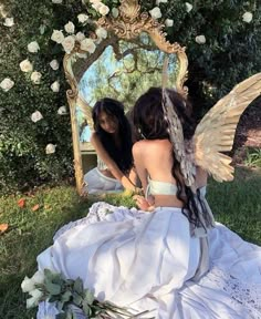 two women sitting in front of a mirror with angel wings on their backs and one holding a flower