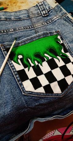 a pair of blue jean pants with a green monster painted on the back and checkerboard pattern