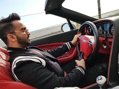 a man sitting in the driver's seat of a red sports car with his hands on the steering wheel