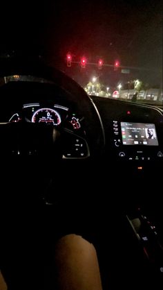 the interior of a car at night with traffic lights in the background and someone's hand on the steering wheel