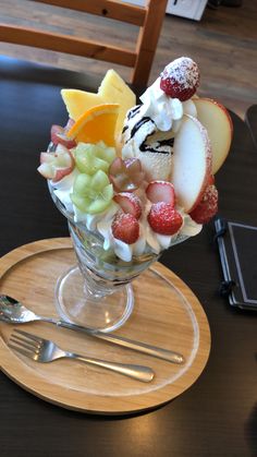 a glass bowl filled with fruit on top of a wooden plate next to a fork