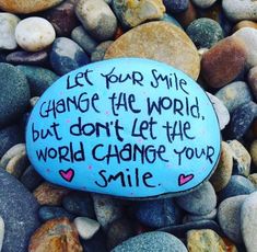 a rock with writing on it sitting among some rocks and stones that say, let your smile change the world but don't let the world change your smile