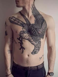 a man with an eagle tattoo on his chest is standing in front of a wall