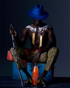 a man sitting on top of a blue box holding a bottle and wearing a blue hat