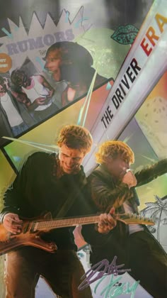 two men are playing guitar together in front of posters