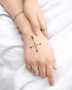 a woman's hand with a cross tattoo on her left wrist, resting on a white sheet