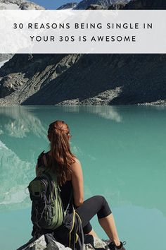 a woman sitting on top of a large rock next to a body of blue water