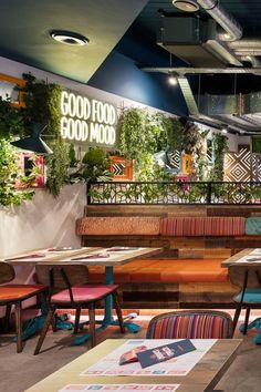 the interior of a restaurant with wooden tables and colorful chairs, plants on the wall