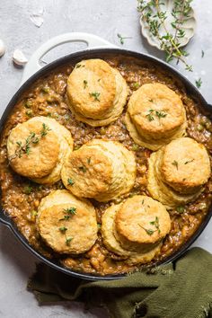 some biscuits are on top of some stew in a skillet with green napkins