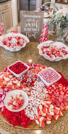 a table topped with lots of food on top of a kitchen counter next to a sign that says love is sweet please take a treat