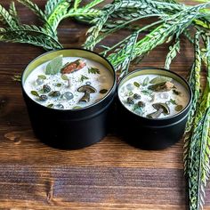 two black containers filled with food sitting on top of a wooden table next to green plants