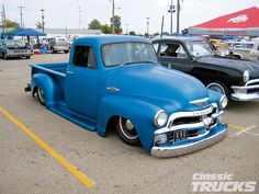 an old blue pickup truck parked in a parking lot next to other classic cars and trucks