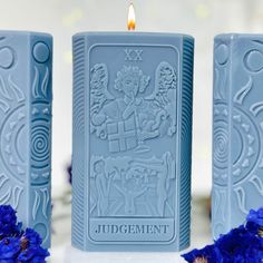 two blue candles sitting next to each other on top of a white table with flowers