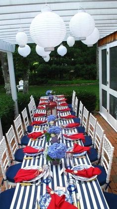 an outdoor dining area with blue and white striped table cloths, red and white placemats, and hanging lanterns