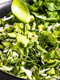 a close up of a spoon in a bowl of food with lettuce and other vegetables