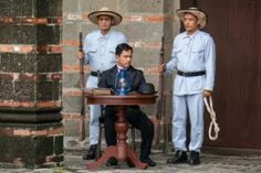 three men in uniforms standing around a table with a man sitting on top of it