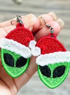 someone is holding up two christmas themed keychains with an alien face on them