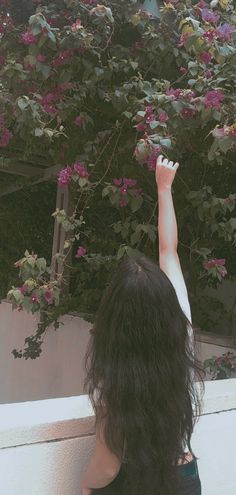 a woman reaching up into the air with her arms in the air while standing next to a tree