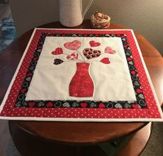 a red vase with hearts on it is sitting on a table next to a white vase