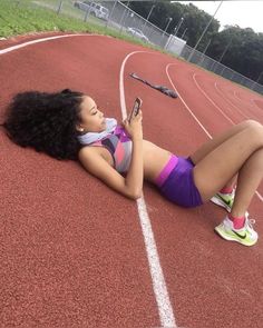 a woman laying on the side of a track with a cell phone in her hand