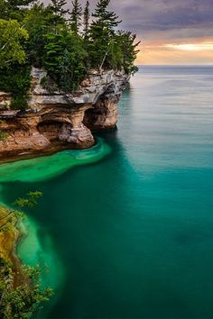 an ocean cliff with green water and trees