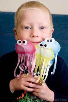 a young boy holding up two jelly fish with googly eyes on it's face