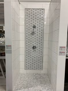 a shower with white tile and silver fixtures in a store display area, showing the back side of the shower