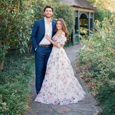 a man and woman standing next to each other in front of some bushes on a path