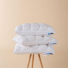 three pillows stacked on top of each other in front of a beige wall and wooden stand