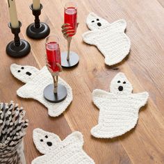 a wooden table topped with white crocheted ghost coasters next to pine cones and candles